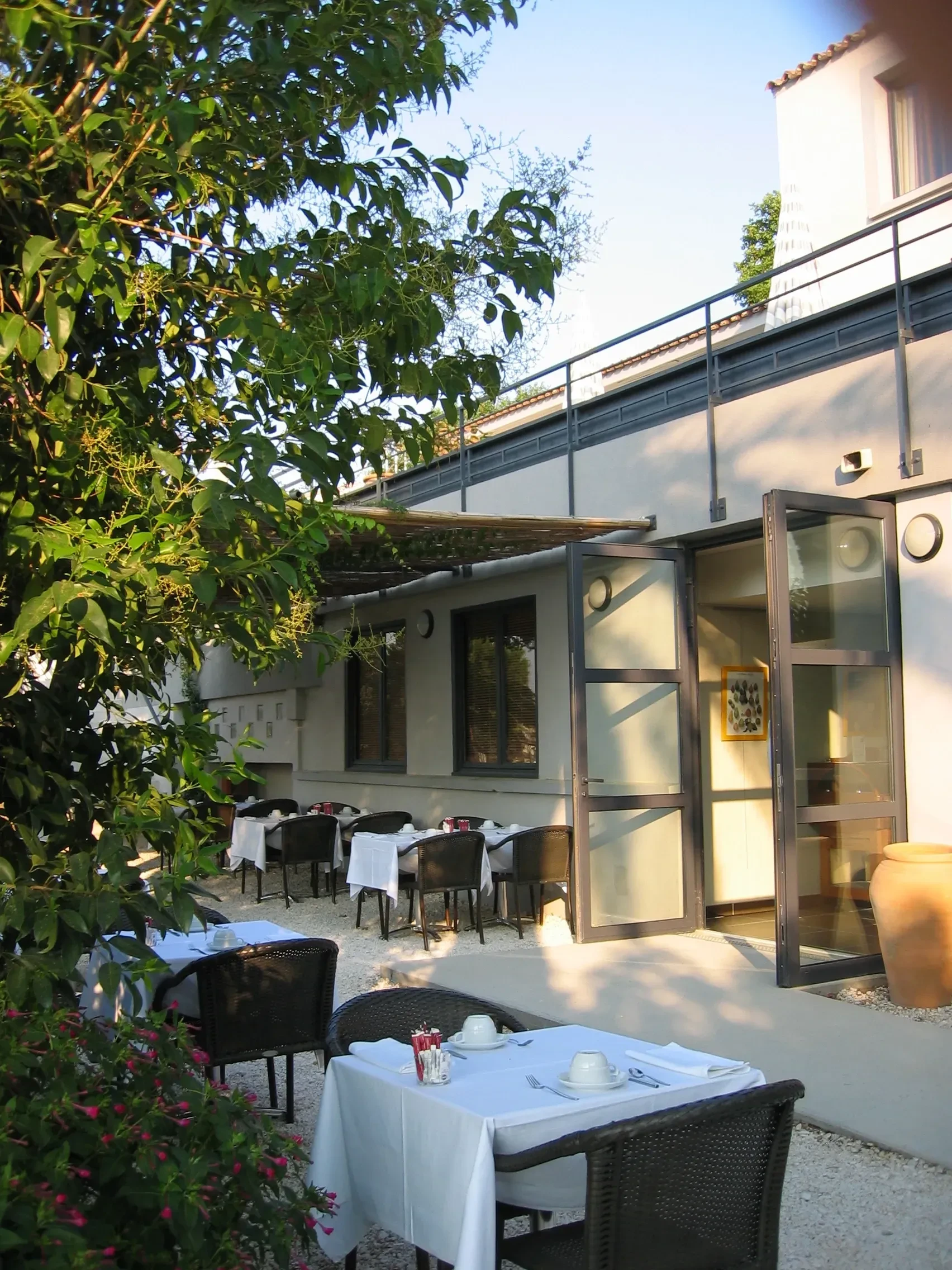 Terrasse de restaurant ensoleillée avec tables dressées, Hôtels Aigues-Mortes Camargue - Les Jardins du Canal